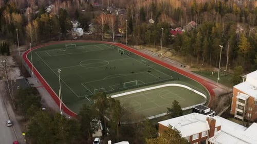 Aerial, tilt down, drone shot towards a team training on a soccer field in Pitajanmaki, during sunse