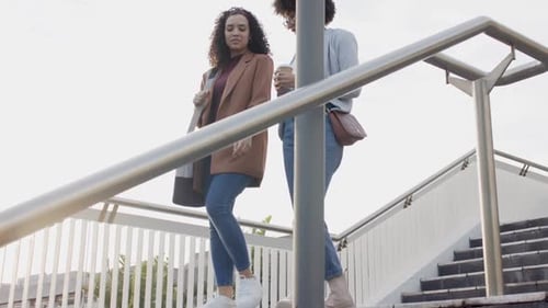 Two Young Women Walk Down Steps Talking Together