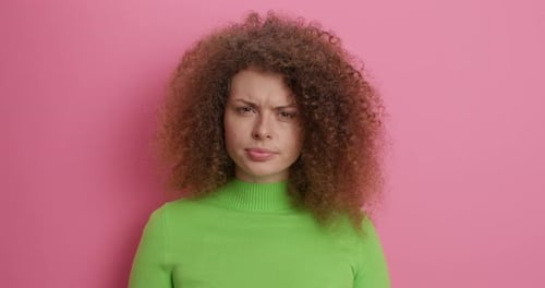 Displeased young woman smirks and expresses negative emotions in studio over pink