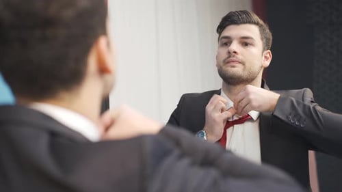 Young Man Adjusting Tie in Front of Mirror