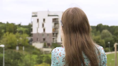 A Beautiful Young Caucasian Woman Talks on a Smartphone As She Looks at an Apartment Complex