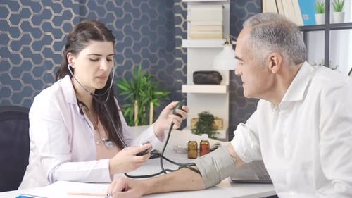 Professional female doctor sitting at office desk and measuring blood pressure of patient.