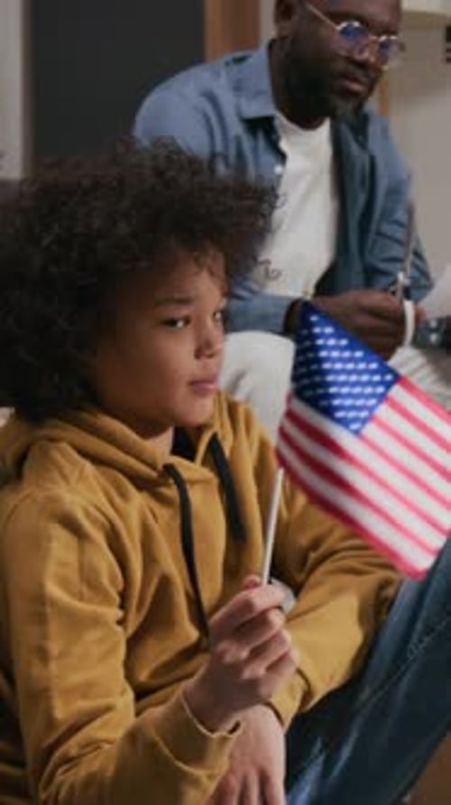 Vertical of Gen Alpha Boy Waving Small US Flag and Showing It to His Father