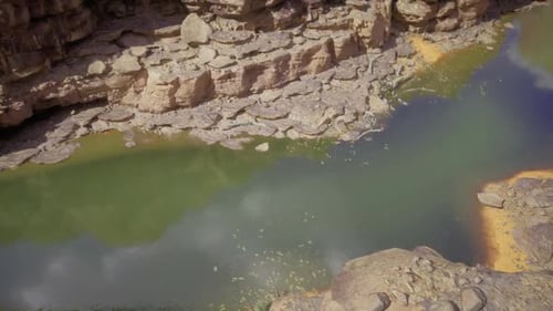 Des silhouettes aviaires se reflètent sur la surface verte d'une rivière au milieu des côtes rocheuses