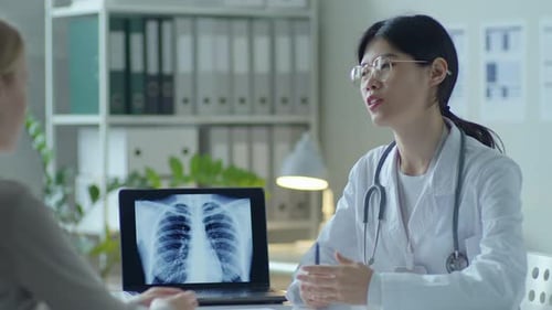 Asian Female Doctor Explaining Chest X-Ray on Laptop to Patient in Clinic