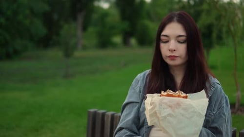Woman Enjoying a Sandwich Outdoors on Park Bench