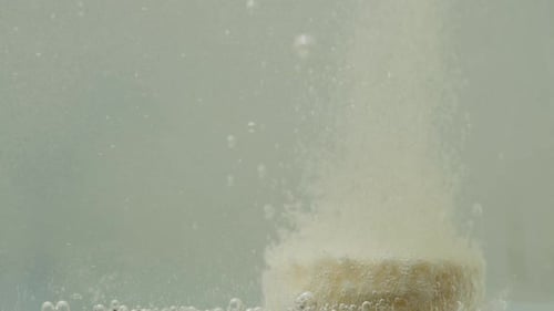 The yellow effervescent tablet dissolves at the bottom, the bubbles rise up. Macro slow motion.