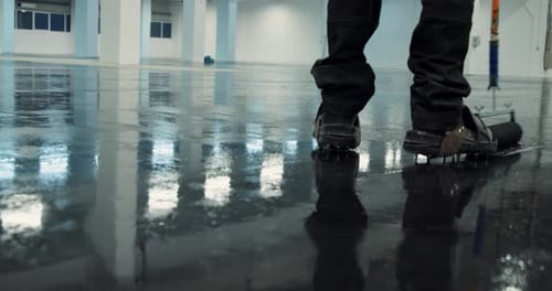 professional worker expertly applies an epoxy flooring layer inside a warehouse using a needle rolle