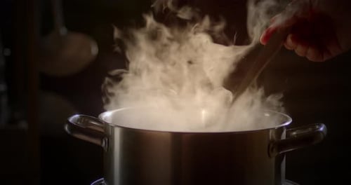 Slow motion scene of a boiling pot steams up as a restaurant's chef uses a ladle to stir soup