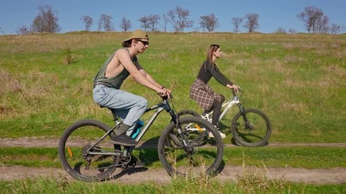 Young Couple Biking on a Green Grassy Hill