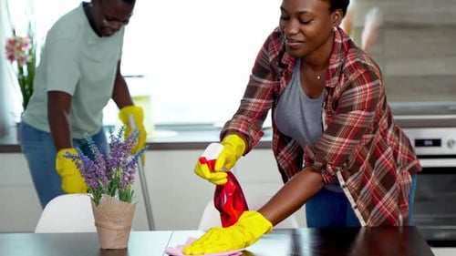 Woman Cleans Table as Man Mops in Background