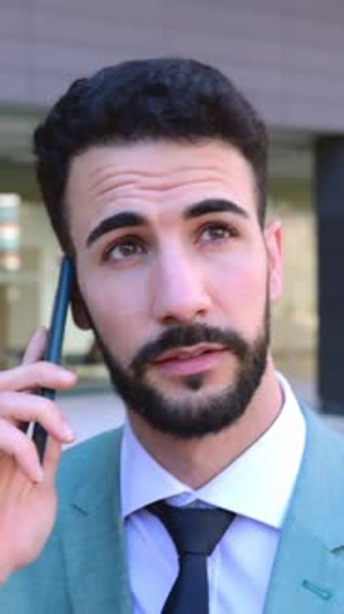 Successful Young Businessman Talking on Mobile Phone While Walking in the Street