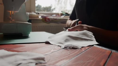 Person Cutting Fabric with Scissors at Table