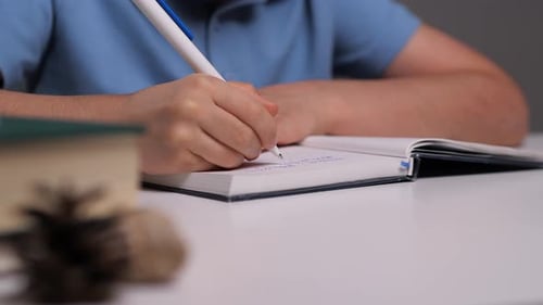 Child Writing in Notebook with Pen at Desk