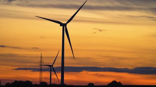 Windturbinen drehen sich in der Abenddämmerung bei unglaublich vielfarbigem bewölktem Sonnenuntergang am Abend