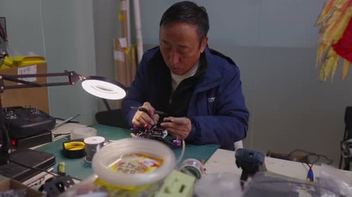 Asian Technician Assembling Quadcopter Parts at Factory Workstation Performing Precise Installation