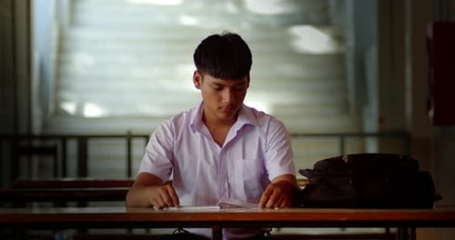 A male high school student in a white school uniform is sitting and studying alone