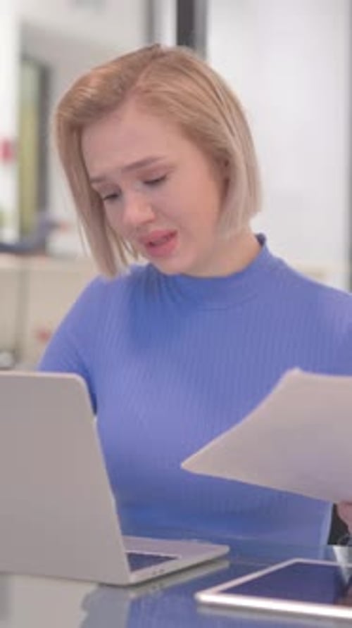 Worried Woman Reviewing Documents at Desk with Laptop