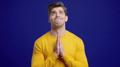 Young Man Praying With Fingers On Blue Background Guy Begs Satisfy Desires