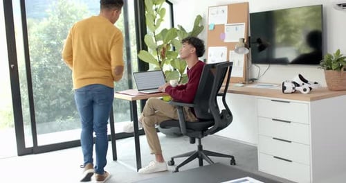 Discutant du travail, couple gay multiracial utilisant un ordinateur portable et une tablette dans un bureau à domicile moderne