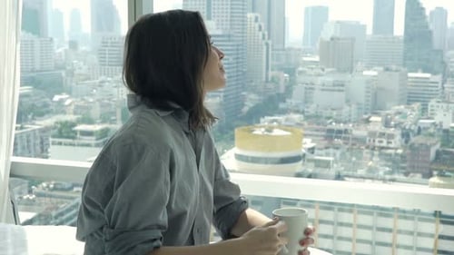 Young, Happy Woman Drinking Coffee on Bed and Admire View From Window