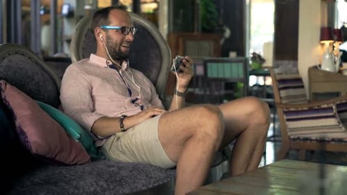 Happy, Young Man Watching Movie On Smartphone Sitting In Trendy Cafe