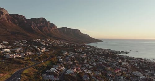 Drone is flying high and backwards over Camps Bay in Cape Town, South Africa - in the distance Table