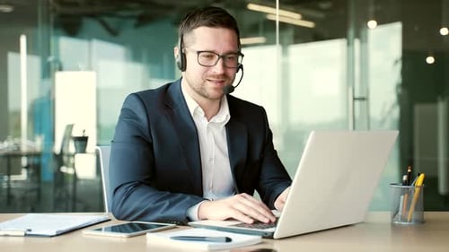 Confident businessman in a headset talking on a video call sitting at a workplace in office.