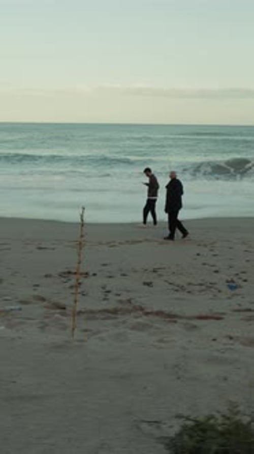 Sur une longue plage, deux personnes marchent en regardant la fureur des vagues de l'océan