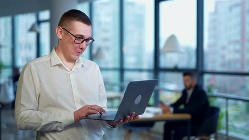Man Smiling Holding Laptop in Modern Office