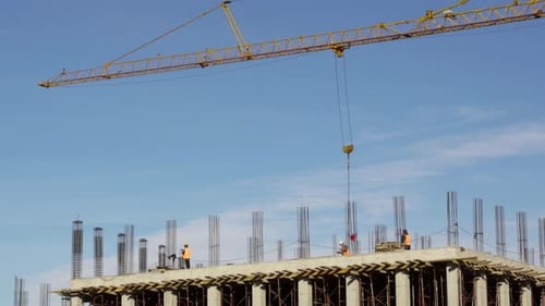 Construction site with workers over terrace loading tower crane ballet with bricks on blue sky backg