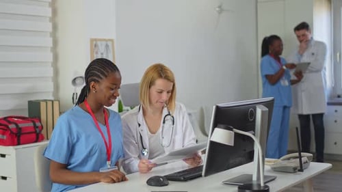 Doctora y enfermera discuten el historial del paciente en una concurrida oficina de un hospital