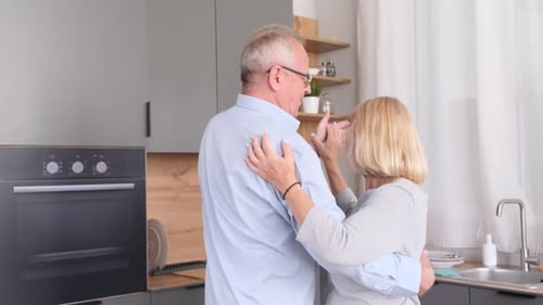Come comida deliciosa y ríe: pareja mayor baila mientras cocina en la cocina de casa