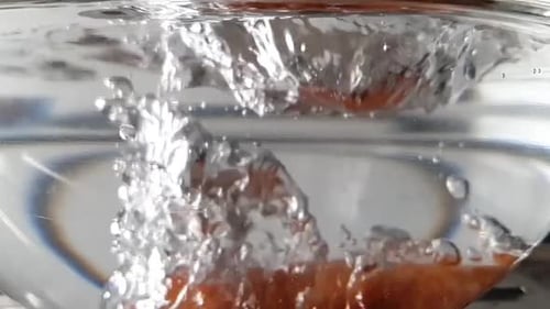 Dropping carrot in the bowl full of water in super slowmotion with water splashing. Bubbles coming o