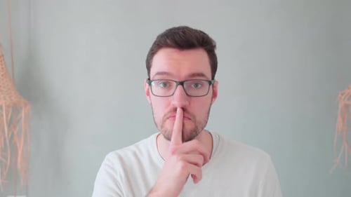 Junger Mann, Finger vor dem Mund, Zeichen der Ruhe, Verschwiegenheit, geheim halten, nicht erzählen, keinen Lärm machen