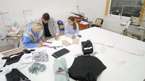 Group of Three Diverse Fashion Dressmakers Looking at Fabric Samples and Discussing Ideas for
