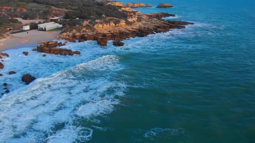Beautiful aerial drone reveal shot of low tide waves crashing the shoreline, located in coastal city