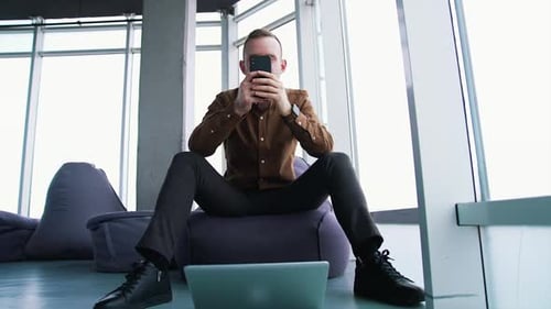 Young man with a phone in office. Handsome businessman sitting on a comfortable armchair