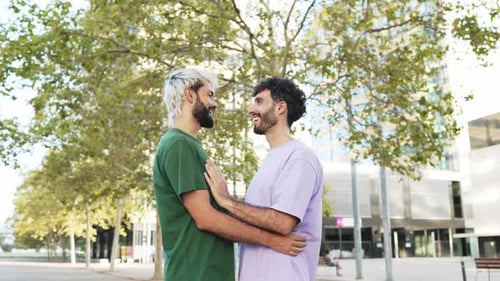 Young gay couple talking to each other hugging and kissing in the street in daylight.