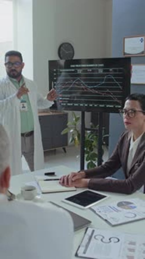 Doctor Presenting Charts on Screen to team at Meeting in Clinic