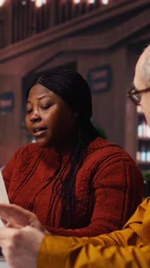 Vidéo verticale : une équipe d'interprètes matures répétant un dialogue scénarisé ensemble dans une bibliothèque