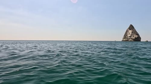 Sea Water Surface Camera Flies Over the Calm Azure Sea with Volcanic Rocky Shores on Background