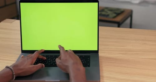 Closeup of a Man Hands Uses Laptop with Green Mockup Screen While Sitting at the Desk in Cozy