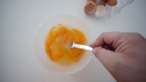 Whisking Egg Yolks With Fork In Bowl Top View With Broken Egg Shells In Background