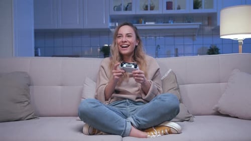 Woman playing video game on sofa at night