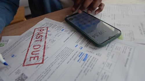 Man Checking Expenses on Smartphone Calculator While Managing Bills at Home