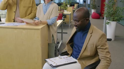 Manager in Wheelchair Giving Documents to Coworkers