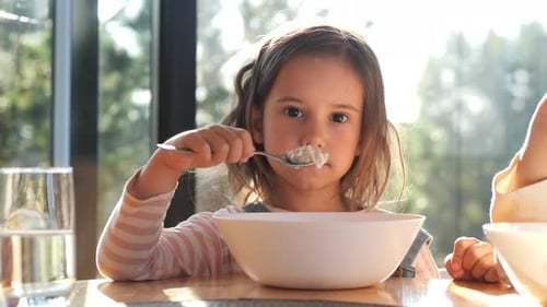 Cute Little Girl Eating Cereal From a White Bowl