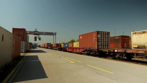 Freight train with colorful containers at a commercial dock during daytime, clear blue sky