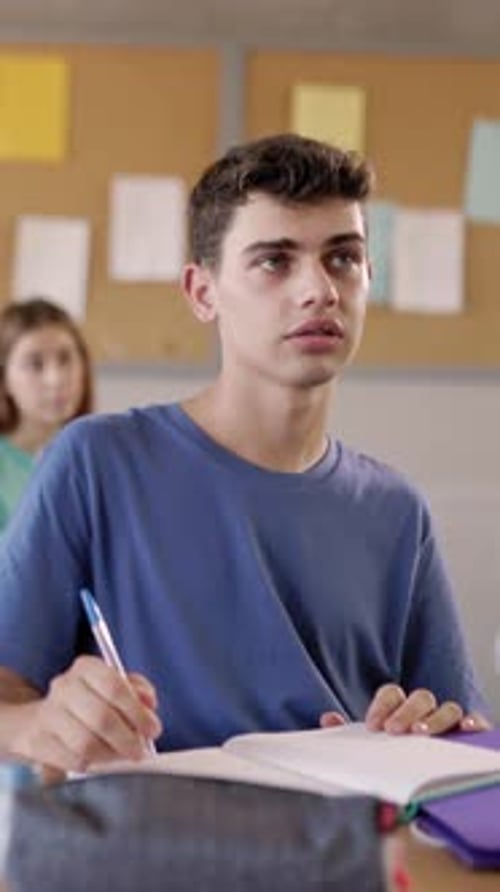 Young Caucasian Student Boy Listening Teacher in Classroom at School